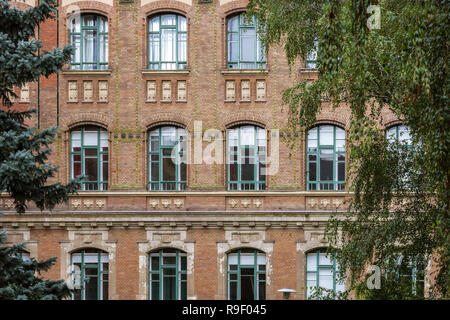 Bogenfenster auf der Mauer, auf dem Campus der Budapester Universität für Technologie und Ökonomie durch Baum Blätter eingerahmt. Stockfoto