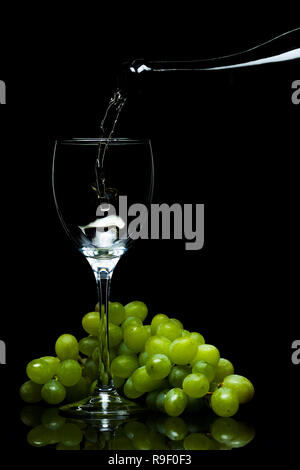 Weißwein aus einer Flasche in ein Glas, ein Bündel von Trauben, einen schwarzen Hintergrund, Studio Light Stockfoto
