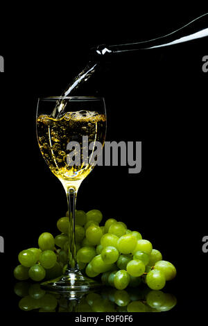 Weißwein aus einer Flasche in ein Glas, ein Bündel von Trauben, einen schwarzen Hintergrund, Studio Light Stockfoto