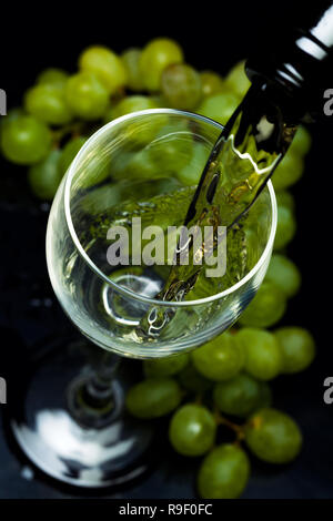 Weißwein aus einer Flasche in ein Glas, ein Bündel von Trauben, einen schwarzen Hintergrund, Studio Light Stockfoto