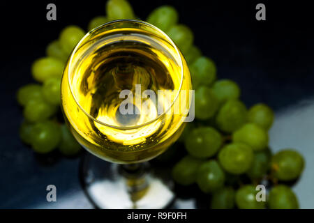 Weißwein aus einer Flasche in ein Glas, ein Bündel von Trauben, einen schwarzen Hintergrund, Studio Light Stockfoto