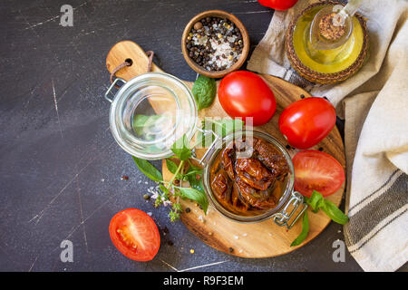 Sonnengetrocknete Tomaten mit Olivenöl in einem Glas auf schwarzen Stein oder Beton. Ansicht von oben flach Hintergrund. Kopieren Sie Platz. Stockfoto