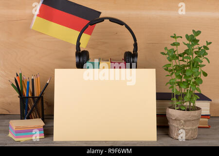 Das Konzept des Lernens der deutschen Sprache - leeres Papier, Flagge der Deutschland, Bücher, Kopfhörer, Bleistifte auf hölzernen Hintergrund Stockfoto