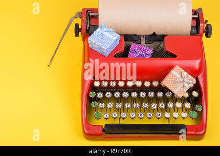 Urlaub Konzept - rot Schreibmaschine mit leeren Handwerk Papier, Geschenkboxen auf gelbem Hintergrund Stockfoto