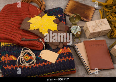 Das Konzept der Herbstferien - Ahorn Blätter, Kompass, Reisepass, Schlüssel mit leeres Etikett, Geschenkboxen, Portemonnaie, warme Kleidung: eine Mütze, Schal, Pullover und g Stockfoto