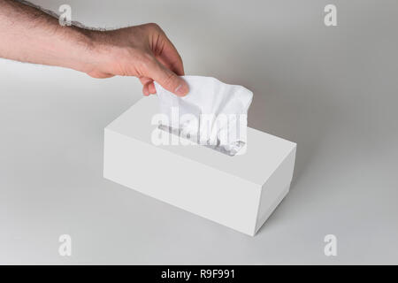 Männer Hand ziehen ein Gewebe aus der weißen leere Tissue Box auf grauem Hintergrund, Gewebe für Print Design und Verpackung mock up, Gesichter Beschneidungspfad enthalten. Stockfoto