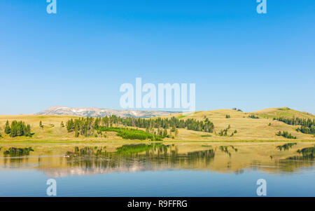 Blick auf den See von Ausläufern der Rocky Mountains unter einem blauen Himmel im Sommer in der Nähe von West Yellowstone, Wyoming, USA flankiert. Stockfoto