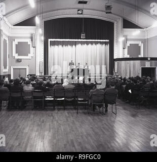 1965, Menschen in einer öffentlichen Sitzung Sitzung zu hören Lautsprecher auf einem Panel auf der Bühne der Borough Assembly Hall (BAH), Aylesbury, Bucks, England, UK. Stockfoto