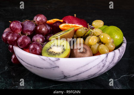 Korb mit frischen tropischen fruitson in Schüssel auf schwarzem Marmor Hintergrund. Ananas, Papaya, Mango, Kiwi, Trauben, Granat, Mandarinen, Bananen, Äpfel, ... Stockfoto