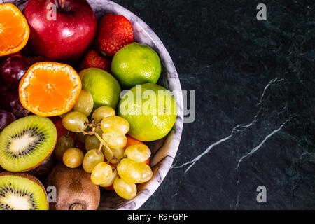 Frische tropische fruitson in Schüssel auf schwarzem Marmor Hintergrund. Ananas, Papaya, Mango, Kiwi, Trauben, Granat, Mandarinen, Bananen, Äpfel, Wassermelone sli Stockfoto