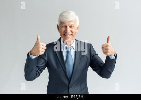 Senior Business mann Studio stehen auf graue Wand zeigen isolierte Daumen hoch suchen Kamera lächeln positive Stockfoto