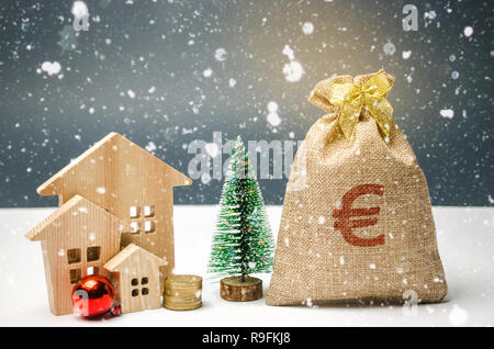 Holzhäuser und Weihnachtsbaum und einen Sack Geld. Weihnachten Verkauf von Immobilien. Neues Jahr Rabatte für den Kauf Haus. Kauf Wohnungen auf einem niedrigen Stockfoto