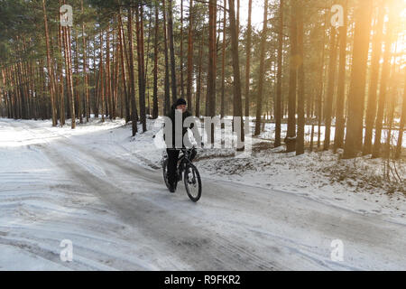 Radfahrer ohne Helm reitet auf schneebedeckten Wald Straße auf dem Fahrrad an sonnigen Frühlingstag. Stockfoto