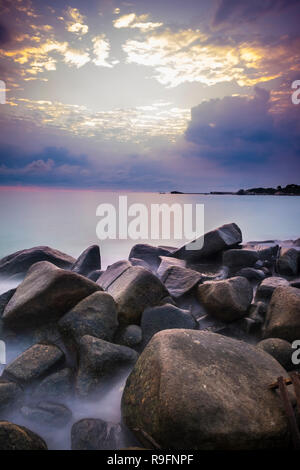 Sonnenaufgang an der Insel Bintan. Sand meer himmel wolken und Steine Stockfoto