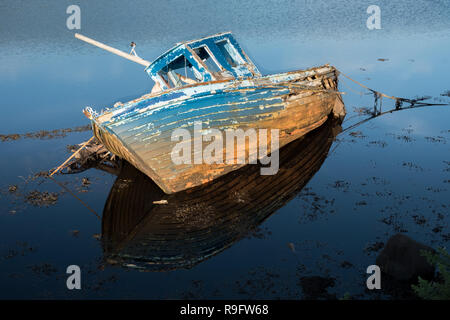 Wrack eines Fischerboot auf den wilden Atlantik Küste von Irland. Verblasste Farbe blau Schiff seitlich liegend mit perfekten Reflexion in Ebbe Wasser. Stockfoto