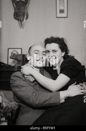 1950er Jahre, ein Paar in einem Stuhl sitzend umarmen, eine lächelnde junge Frau mit ihrem Arme um ihre männlichen Liebhaber, ein älterer Mann. Stockfoto