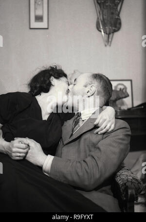 1950er Jahre, ein paar Küssen, ein älterer Mann mit einer jüngeren Frau zusammen auf einem Stuhl sitzend, England, UK. Stockfoto