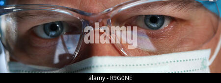 Stattliche männliche Arzt Gesicht durch das Tragen von schützender Maske Stockfoto