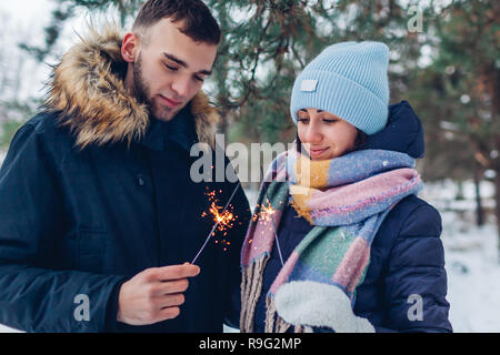 Schöne liebevolle Paar brennende Wunderkerzen im Winter Wald. Weihnachten und neues Jahr feier Konzept Stockfoto