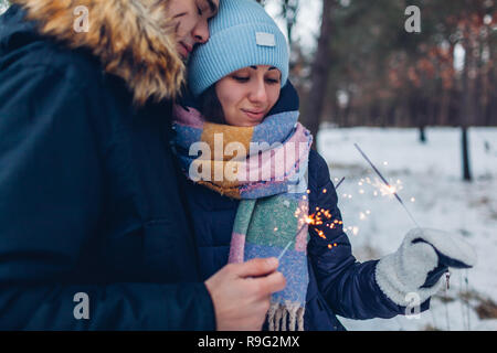 Schöne liebevolle Paar brennende Wunderkerzen im Winter Wald. Weihnachten und neues Jahr feier Konzept Stockfoto