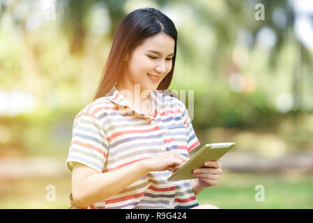 Gerne Frau mit Touchpad/Schöne junge Mädchen lächelnd suchen Tablet für Unterhaltung und Kommunikation auf der Park im Freien - glückliche Frau student Stockfoto