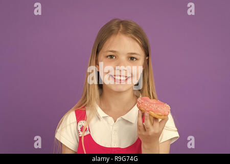 Kind Lächeln mit Donut auf Violett Hintergrund. Kleines Mädchen mit glasierten ring Donut. Glückliches Kind mit Junk Food auf lila Hintergrund. Essen und Nachtisch. Kindheit und Kinderbetreuung. Stockfoto