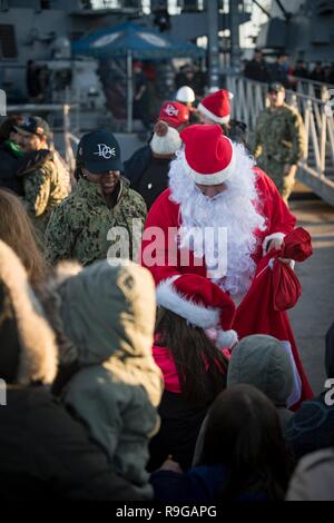 Rota, Spanien. 22 Dez, 2018. U.S. Navy sailor 1. Klasse Robert Camphouse, verkleidet als Weihnachtsmann, bietet Geschenke warten auf Familienmitglieder als Matrosen von Bord der Arleigh-Burke-Klasse geführte Anti-raketen-Zerstörer USS Donald Cook als das Schiff bei Naval Station Rota Dezember 22, 2018 in Rota, Spanien ankommt. Credit: Planetpix/Alamy leben Nachrichten Stockfoto