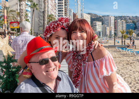 Benidorm, Costa Blanca, Spanien, 24. Dezember 2018. Britische Urlauber die Flucht aus der Kälte nach Hause Flut das beliebte Resort in den Weihnachtsferien mit der Familie geschmückt in Lametta und tragen Christbaumkugel Ohrringe erhalten in der Stimmung für die Festlichkeiten. Sonnenanbeter und Schwimmer genießen Sie die heißen temps und ruhigem Wetter am Strand Levante heute in Benidorm an der Costa Blanca Küste. Die Temperaturen waren in den mittleren bis hohen 20 Celsius heute in diesem mediterranen Hotspot. Credit: Mick Flynn/Alamy leben Nachrichten Stockfoto