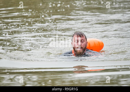 Fluss Nene, Northamptonshire, Großbritannien. 25. Dez 2018. Gekleidet in einen Neoprenanzug und Schwimmweste im Schlepptau, ein Mann mittleren Alters nimmt eine im kalten Wasser des Flusses Nene am Weihnachtstag 2018 schwimmen. Quelle: Michael Foley/Alamy leben Nachrichten Stockfoto