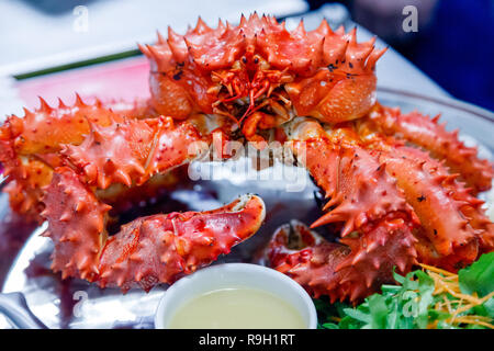 Nahaufnahme von lecker lecker gekocht Frisch rote Königskrabben auf Metall Teller mit Zitrone, gruene Sauce zubereitet. Konzept teures Essen, Schmuggel, vip-Lieferung Stockfoto