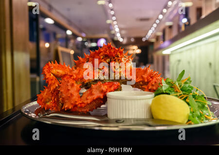 Nahaufnahme von lecker lecker gekocht Frisch rote Königskrabben auf Metall Teller mit Zitrone, gruene Sauce zubereitet. Konzept teures Essen, Schmuggel, vip-Lieferung Stockfoto