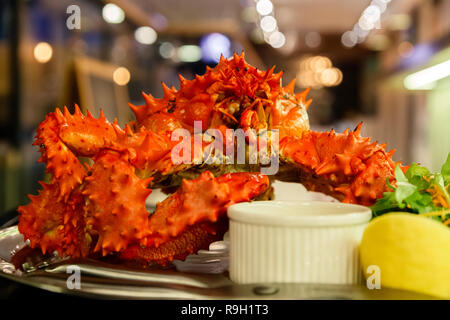Nahaufnahme von lecker lecker gekocht Frisch rote Königskrabben auf Metall Teller mit Zitrone, gruene Sauce zubereitet. Konzept teures Essen, Schmuggel, vip-Lieferung Stockfoto