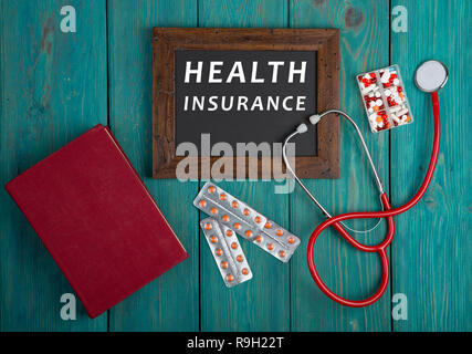 Tiermedizin Konzept - Tafel mit Text "Krankenversicherung", Buch, Pillen und Stethoskop auf Blau Holz- Hintergrund Stockfoto