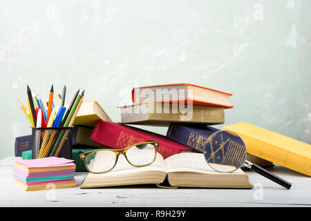 Einen Stapel alte Farbe Bücher, Gläser, Bürobedarf und Lupe auf eine Tabelle und ein grüner Hintergrund Stockfoto