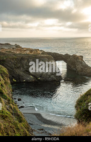 Rock arch und das robuste Pacific bei Sonnenuntergang mit dramatischen Wolken Stockfoto