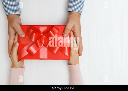 Nahaufnahme eines Menschen Hand ein rotes Kästchen mit einem Geschenk für eine Frau. Ansicht von oben. Konzept der Valentinstag und Weihnachtsfeier Stockfoto