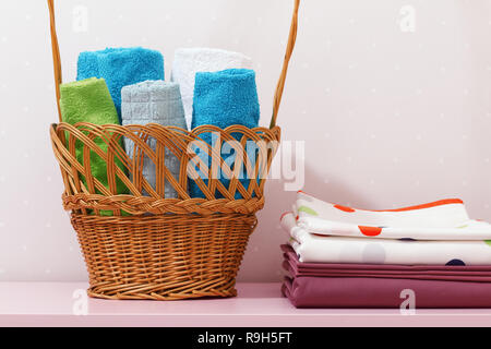 Auf der Kommode gibt es einen Stapel sauber gebügelte Bettwäsche und es gibt einen Korb in Rollen der gefalteten Bunte Handtücher. Stockfoto