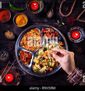 Frau essen Vegetarische biryani durch ihre Hand mit Armreifen in der Nähe von Kerzen, Weihrauch und religiöse Symbole in Diwali Feier Stockfoto