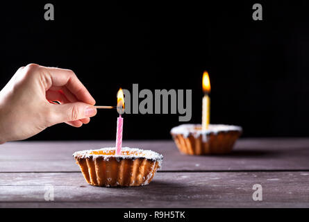 Hand Anwendung übereinstimmen, um eine Kerze auf käsekuchen auf schwarzem Hintergrund Stockfoto