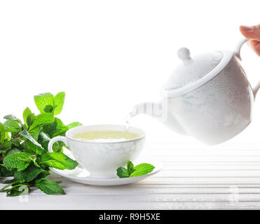 Pfefferminztee Ausgießen von Teapot in der Tasse in der Nähe von Minze auf weißem Hintergrund Stockfoto