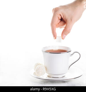 Frau hand Zucker im schwarzen Tee in weiße Tasse mit zwei Süßen Kokos Kugeln auf weißem Hintergrund Stockfoto