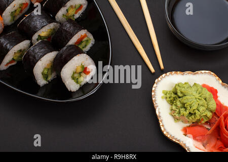 Sushi Rollen in Nori Algen Blätter mit Avocado und rote Fische auf Keramikplatte. Mit roten eingelegten Ingwer und Wasabi. Schüssel mit Sojasauce und Woode Stockfoto