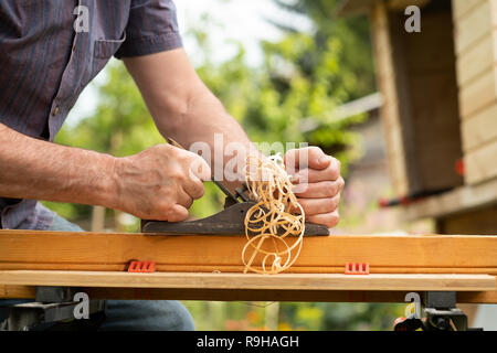 Die Hände eines Zimmermanns gehobeltes Holz im Freien im Sommer Stockfoto