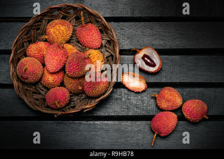 Litschi Früchte auf einem Weinstock hölzerne Schüssel auf einem schwarzen dunklen Hintergrund closeup Stockfoto