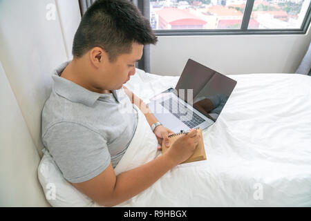 Asiatische Journalist schriftlich auf Notebooks im Schlafzimmer Stockfoto