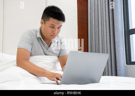 Asiatischer mann Arbeiten am Laptop im Schlafzimmer Stockfoto