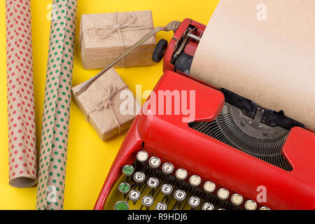 Urlaub Konzept - rot Schreibmaschine mit leeren Handwerk Papier, Geschenk, Kästen und Verpackung Papier auf gelbem Hintergrund Stockfoto