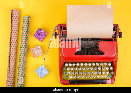 Urlaub Konzept - rot Schreibmaschine mit leeren Handwerk Papier, Geschenkboxen auf gelbem Hintergrund Stockfoto