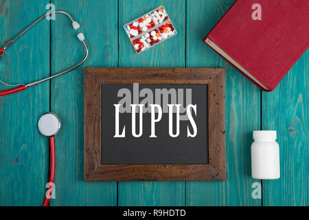 Tiermedizin Konzept - Tafel mit Text "Lupus", Buch, Pillen und Stethoskop auf Blau Holz- Hintergrund Stockfoto