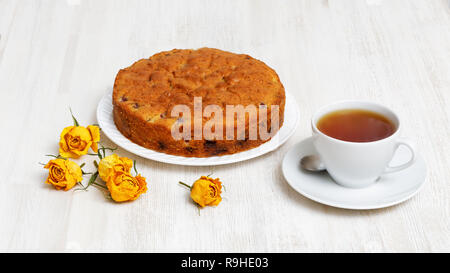 Hausgemachte pear-Torte mit Schokolade und Kirschen, Tasse Tee und getrocknete gelbe Rosenblütenblätter auf weissem Holztisch Stockfoto